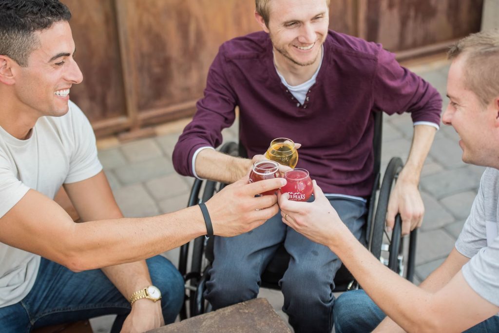 Three smiling men in wheelchairs sharing drinks. 