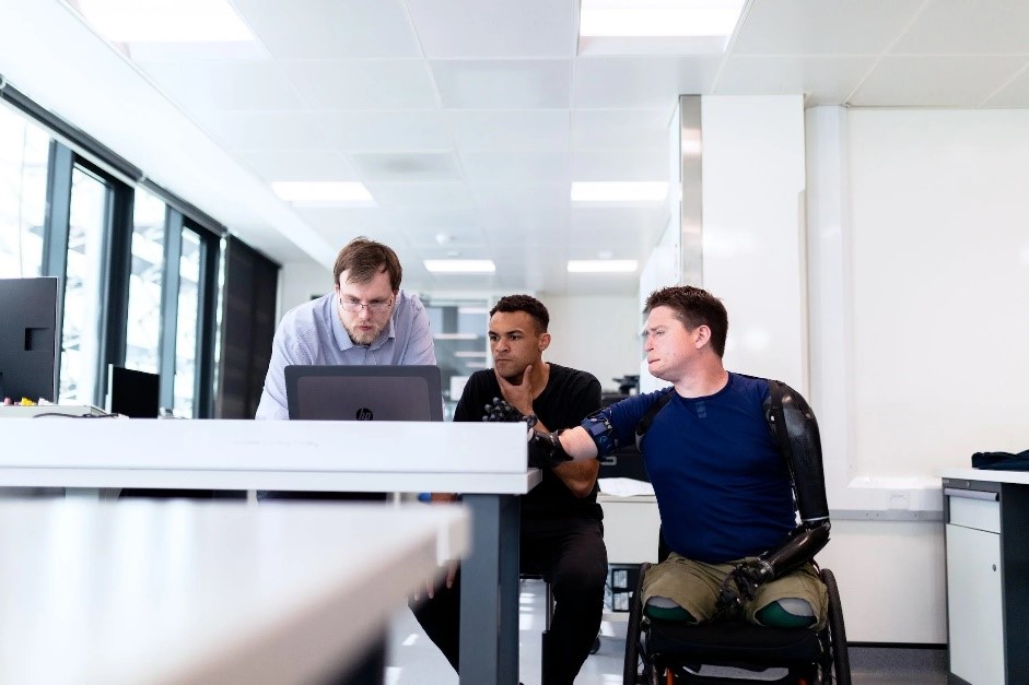 A man in a wheelchair discussing with two men over a laptop. 