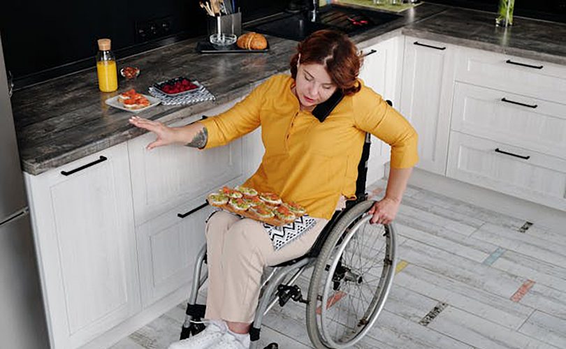 Image Description: A woman sitting in a wheelchair in the kitchen. Image Credit: https://www.pexels.com/photo/woman-in-yellow-long-sleeve-shirt-sitting-on-wheelchair-4063512/