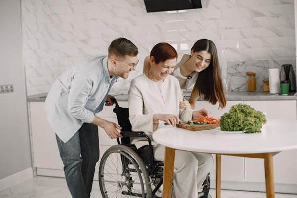 Family supporting a woman in a wheelchair while cooking in a kitchen, showing the importance of customising temporary housing during a move for accessibility and comfort. https://www.pexels.com/photo/women-and-man-with-vegetables-on-table-in-kitchen-7446746/