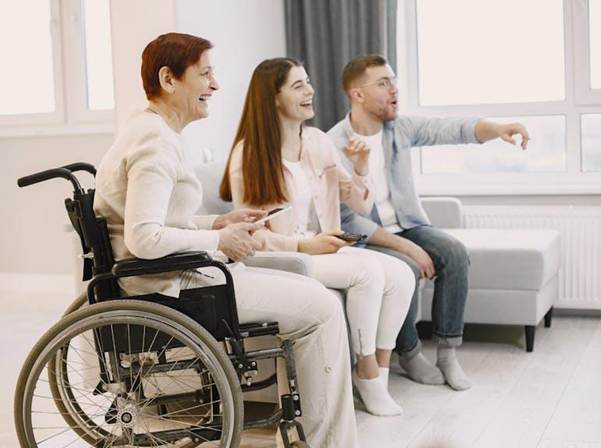 Image Description: A person in a wheelchair next to a sofa. Image Credit: https://www.pexels.com/photo/elderly-woman-on-a-wheelchair-spending-time-with-family-7446771/