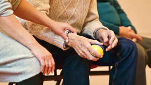 Image Description: An older person sitting next to the caregiver. Image Credit: https://www.pexels.com/photo/person-holding-a-stress-ball-339620/ Matthias Zomer