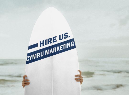 Image Description: Brown & Cream Coloured Image Depicting a Typewriter With Wording "Hire Us. Cymru Marketing". Typed On Paper. Image Credit: PhotoFunia.com Category: Vintage Typewriter.