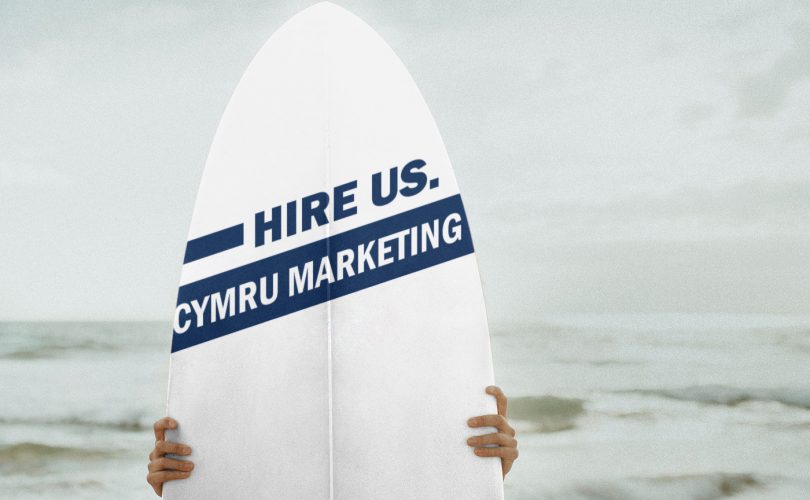 Image Description: Brown & Cream Coloured Image Depicting a Typewriter With Wording "Hire Us. Cymru Marketing". Typed On Paper. Image Credit: PhotoFunia.com Category: Vintage Typewriter.