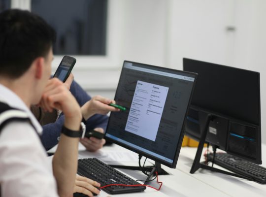Image Description: A group of people sitting at a table with computers. Image Source:https://unsplash.com/photos/a-group-of-people-sitting-at-a-table-with-computers--JUlfa5fAIg?utm_source=unsplash&utm_medium=referral&utm_content=creditCopyText Image Credit: https://unsplash.com/@antoie?utm_source=unsplash&utm_medium=referral&utm_content=creditCopyText
