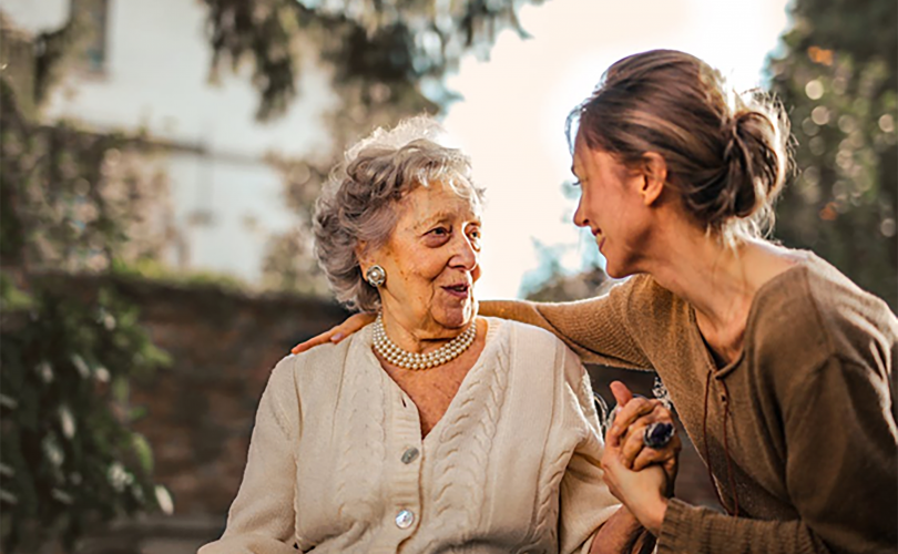 Image Description: Two women sitting together with the younger woman facing the elderly woman and her arm stretched out behind the elderly woman's Back. Image Credit: https://www.pexels.com/photo/3768131/