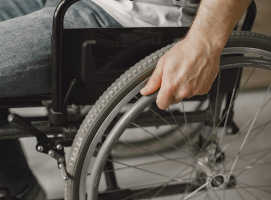 Image Description: A person holding a wheelchair. Image Credit: Gustavo Fring. Image Source: https://www.pexels.com/photo/a-person-holding-a-wheelchair-7446613/