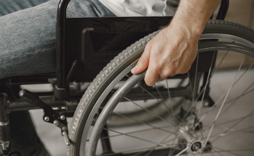 Image Description: A person holding a wheelchair. Image Credit: Gustavo Fring. Image Source: https://www.pexels.com/photo/a-person-holding-a-wheelchair-7446613/