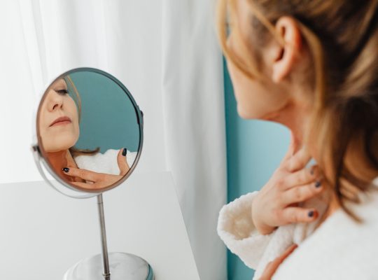 Image Description: Woman Applying Cream To Her Neck In Mirror. Image Credit: https://kaboompics.com/ Image Source: https://www.pexels.com/photo/woman-applying-cream-to-her-neck-in-mirror-7321318/