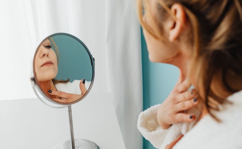 Image Description: Woman Applying Cream To Her Neck In Mirror. Image Credit: https://kaboompics.com/ Image Source: https://www.pexels.com/photo/woman-applying-cream-to-her-neck-in-mirror-7321318/